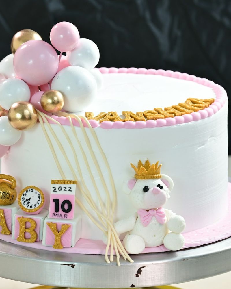 Şeker hamurundan ayıcık, bebek küpleri ve pembe altın balonlar olan beyaz pasta